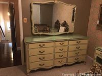Full view of beige ornate dresser with twelve drawers and large matching wall mirror hung above it