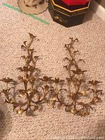 Overhead view of both gold-tone metal sconces laid flat on carpet.