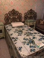Photo of single bed with floral mattress and two ornate wooden headboards with matching nightstands, set against patterned wallpaper.