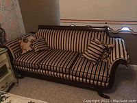 Front view showing the striped upholstery and wooden frame with a floral pillow and striped pillows on the couch.