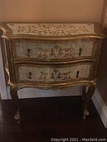 Front left side view of the ornate curio side table showing two curved front drawers and cabriole legs with gold accents.