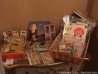 Wicker basket and table display showing assorted vintage stickers, lottery tickets, and postcards organized and packaged.
