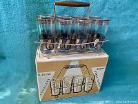 Set of 8 glass tumblers with gold paisley design in brass caddy on original box, sunny blue background