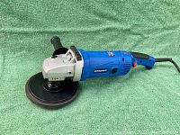 Full side view of the Simoniz blue electric buffer tool showing power cord, handle, and red power switch with padded side handle and buffer pad attached.