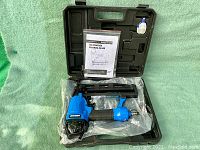 Opened black plastic carrying case showing blue and black Mastercraft finishing nailer placed inside with its manual and a small white plastic container.