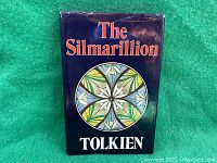 Front cover of The Silmarillion book showing dust jacket with title, author's name, and circular emblem design on dark blue background.