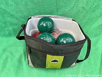 Top open view of carrying bag showing four green bocce balls, red balls, white pallino and plastic bag inside.