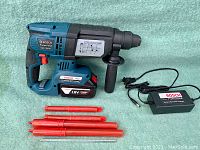 Overall view of drill, battery, charger, handle, red tubes and metal rods laid out