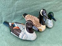 Three vintage wooden duck decoys including pintail, Canada goose, and mallard shown from front and side angles on green fabric background.