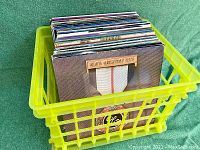 Crate of multiple vintage vinyl records showing album covers arranged vertically in yellow plastic crate.