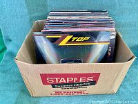 Staples Business Depot cardboard box filled with vinyl LPs, front view shows ZZ Top Eliminator at lead edge