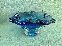 Blue hand blown art glass vase with ruffled rim and clear pedestal base, showing shape and color