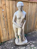 Full view of the life-size Greek style female statue made of cast fiberglass composite, standing on a rectangular base in an outdoor setting against a wood fence.