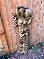 Full view of the large wall sculpture relief leaning against a wooden fence, showing the entire figure and base.