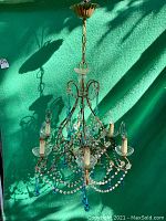 Full view of vintage metal chandelier with six candle-style light sockets, clear glass bowls, clear and blue glass bead garlands, and hanging blue glass drops.