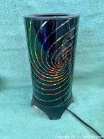 Front view of the cylindrical motion lamp featuring colorful spiral patterns on black body.