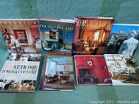 Eight hardcover books on interior design and architecture arranged on a green surface under natural light.