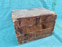 Front view of the vintage wooden crate with closed hinged lid, showing locking slot.