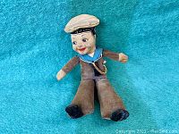 Full view of vintage fabric doll dressed as sailor on turquoise background.