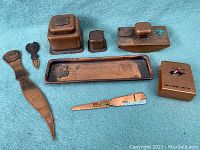 View of all antique copper desk set pieces arranged on blue fabric, showing the variety of desk accessories including letter opener, ink blotter, tray, match holder, and souvenir boxes, all with patina and Calumet Michigan markings.