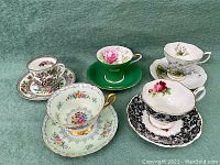 Five tea cup and saucer sets grouped on green felt