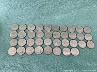 Top image showing 40 silver-colored Canadian quarters arranged in six rows on a green surface. Coins appear worn with varying degrees of tarnish.