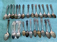 Full collection of 27 antique souvenir spoons arranged in rows, displaying variety of designs and sizes.