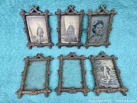 Six antique metal frames laid out on teal fabric, three with black-and-white portrait photos, two empty frames visible with glass intact.