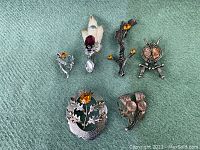 Overview of six vintage Scottish brooches and pins arranged on green fabric