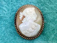 Front view of the antique cameo brooch showing the hand-carved female profile in relief within a twisted rope metal frame.