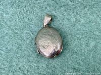 Front view of vintage sterling silver oval locket pendant showing engraved floral design and bail.