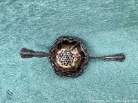 Full top view of the old Birks sterling silver tea strainer showing the perforated and scalloped bowl with detailed ornate edge design and decorated handles on each side.
