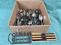 Box filled with antique silverplate flatware including spoons, forks, and knives, showing some wear and tarnish.