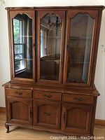Full view of combined cabinet with glass hutch on top, showing wooden construction, glass doors, metal handles, carved wood detail and reflection of room.