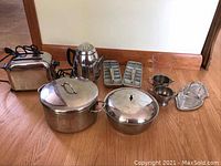 Full set of kitchen items including toaster at back left, electric coffee pot beside it, metal pots in front, two metal ice cube trays in center, glass cream and sugar containers and glass serving tray at right.