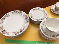 Set of plates, saucers and tea cup with a pink rose and green leaf floral pattern around the edge.