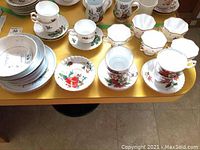 Collection of plates, cups, and saucers displayed on a yellow table, showing floral prints and signs of wear, including chipping.