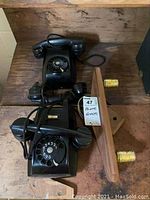 Wide shot showing two vintage black rotary dial telephones on wooden surface alongside wooden wall sconce and spare receiver.