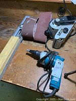 Makita drywall screwdriver and Miller Falls belt sander on wooden surface with sanding belts nearby