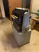 Side and angled view of Moody and Sons planer machine showing its size and structure with large handwheel and rollers.