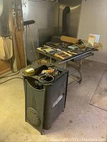 Two-piece Beaver table saw with heavy metal base and flat top section, shown with multiple blades and accessories scattered on top, set in a workshop environment.