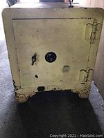 Front view of heavy large safe showing combination lock and handle, scratched paint, heavy hinges, ornate wheels.