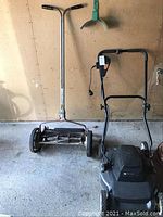 Photo of manual reel push mower and Black & Decker electric mower side by side against wall.