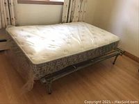 Side view of mattress on metal bed frame, showing mattress larger than frame