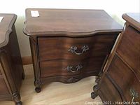 Front view of wooden side table showing two drawers with ornate handles and carved details.