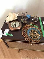 Overview shot showing the kettle clock, wall hangings, table clocks, bird figurines, and conch shell on a dark table surface