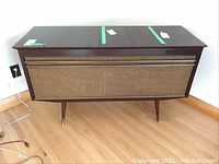 Front angled view of the Edison audio cabinet showing wood finish, speaker grill, and storage doors taped shut.