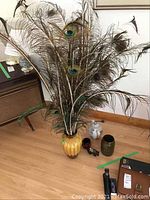 Photo showing the full lot on the floor including the yellow ceramic vase with attached peacock feathers, smaller vases, cup, bear figurine, and teapot.