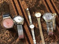Six male and female wristwatches with variety of bands and faces on carpet