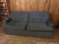 Front view of green upholstered sofa bed showing its button-tufted cushions, rolled arms, and skirted base.